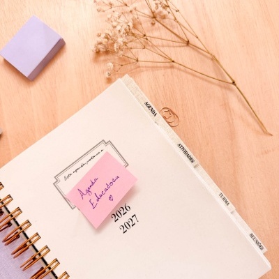 Agenda branca de espiral com separadores, nota rosa, flores secas e cristal sobre mesa de madeira
