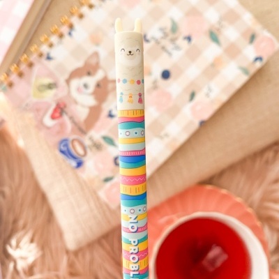 Lápis colorido com borracha em forma de lhama e caderno de capa quadriculada ao fundo