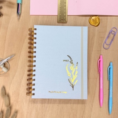 Caderno azul com detalhes dourados e papelaria sobre mesa de madeira