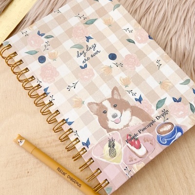 Caderno com capa xadrez bege e branco decorada com flores e cão, espiral dourada, lápis amarelo e tapete bege peludo