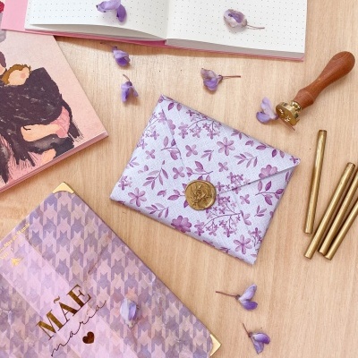 Carteira floral lilás em mesa com cadernos e flores lilás espalhadas