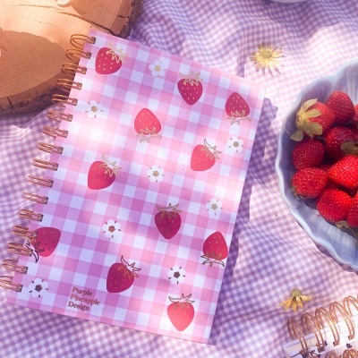 Caderno rosa xadrez com morangos sobre toalha lilás xadrez e frutas em tigelas