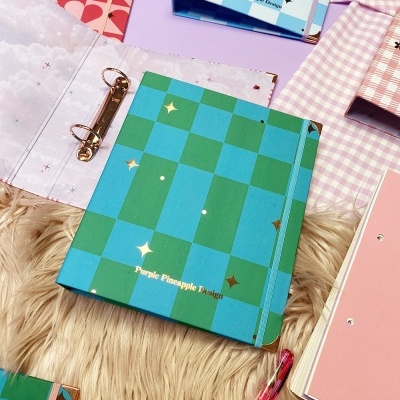 Pasta de argolas verde e azul com padrão quadriculado e estrelas douradas