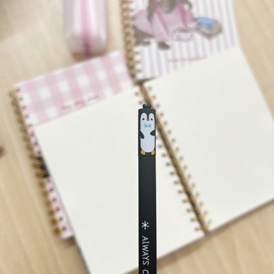 Lápis preto com pinguim e texto Always Cool sobre mesa com cadernos e estojo