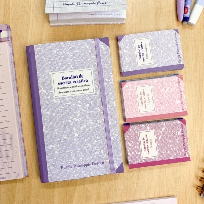 Conjunto de cadernos e baralhos de escrita criativa em várias cores sobre mesa de madeira.