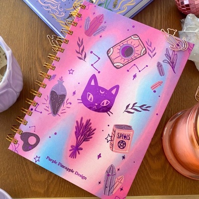 Caderno espiral rosa com ilustrações místicas e texto Purple Pineapple Design