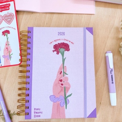 Agenda 2026 lilás com espiral dourada e ilustração de mão segurando flor rosa