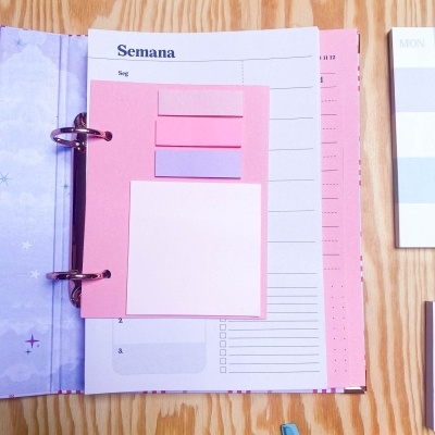 Agenda aberta com post-its rosa e lilás sobre página da semana em português