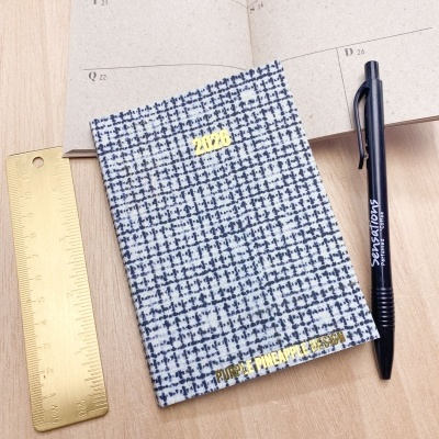 Agenda 2026 com capa azul e branca e texto dourado sobre mesa de madeira com régua dourada e caneta preta