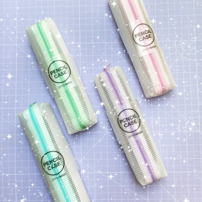 Estojos para lápis brancos com padrão quadriculado e fechos coloridos sobre fundo azul quadriculado.