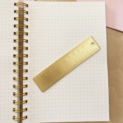Caderno com folhas pontilhadas e régua metálica dourada sobre ele