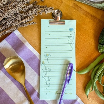 Lista de notas floral presa por clip sobre mesa com utensílios e legumes