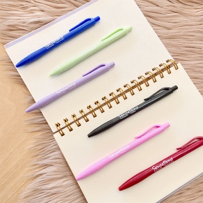 Caderno aberto com seis canetas coloridas alinhadas sobre as páginas