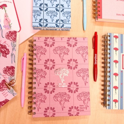 Cadernos espiral com capas florais e canetas coloridas sobre mesa de madeira