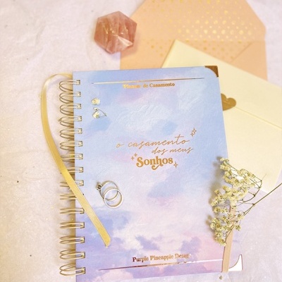 Caderno azul e rosa com texto dourado e acessórios de casamento sobre fundo branco