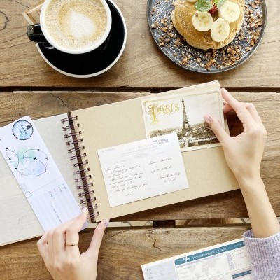 Cappuccino, panquecas com banana e nozes e caderno de viagem sobre mesa de madeira clara