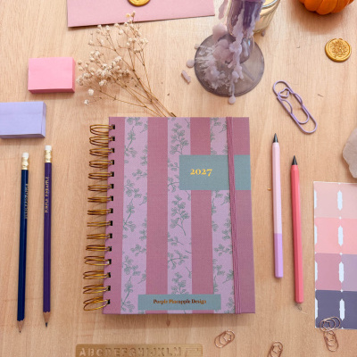 Agenda 2027 floral e riscada com material de escritório e decoração em mesa de madeira