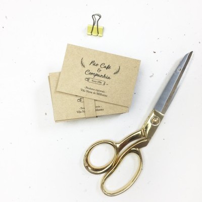 Tesouras douradas, clipe amarelo e cartões marrons com texto pretos sobre superfície branca