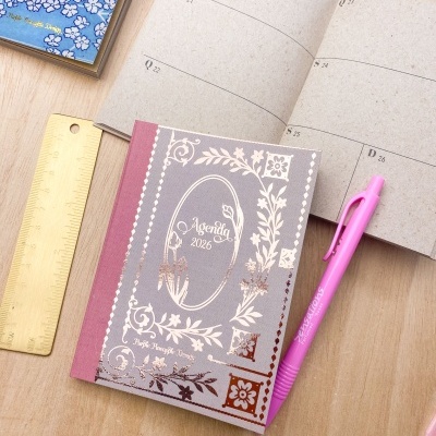 DuAS agendas 2026, régua dourada e caneta rosa numa mesa de madeira clara