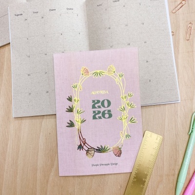 Agenda 2026 rosa com flores douradas sobre mesa com régua e canetas