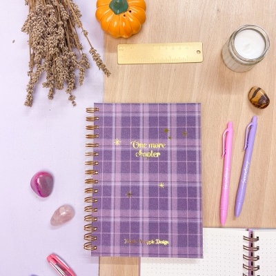 Caderno xadrez roxo com texto dourado e material de escrita e decoração ao redor
