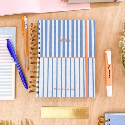 Caderno espiral riscado azul branco com canetas e régua dourada em mesa de madeira