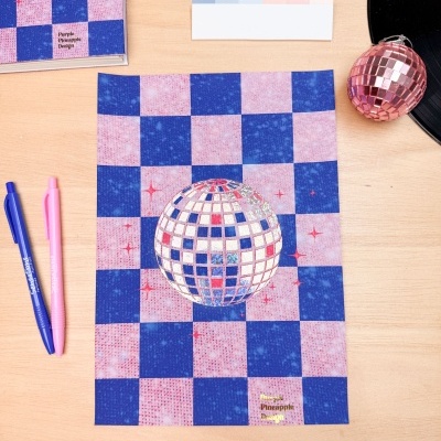 Folha de papel azul e rosa com esfera disco espelhada e vários objetos de papelaria numa mesa de madeira