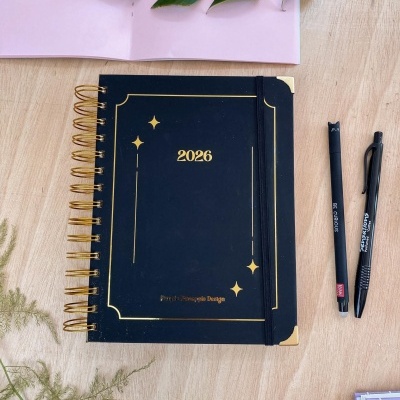 Agenda preta 2026 com caneta preta e régua dourada sobre mesa de madeira