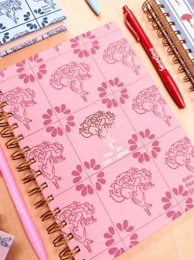 Cadernos espiralados com capas decoradas de flores e canetas coloridas sobre mesa de madeira