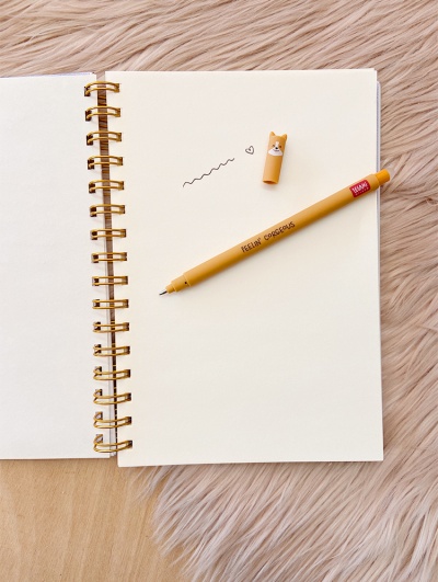 Caderno espiral aberto com caneta amarela e tampa com rosto de cão.
