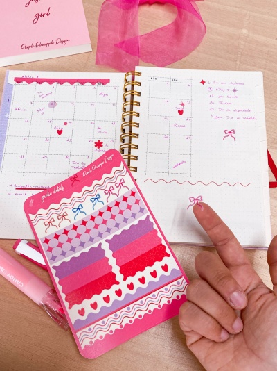 Caderno aberto com anotações e adesivos coloridos rosados e mão apontando
