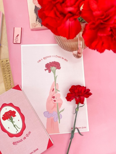 Livro rosa, folha com desenho de mão e cravo e cravo vermelho real num fundo rosa.