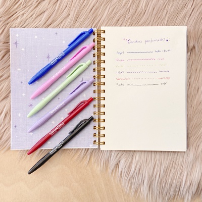 Caderno aberto lilás com canetas coloridas e lista escrita à mão.