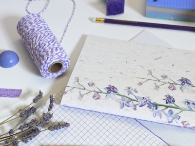 Envelope branco com padrão floral azul e roxo rodeado de acessórios de papelaria roxos