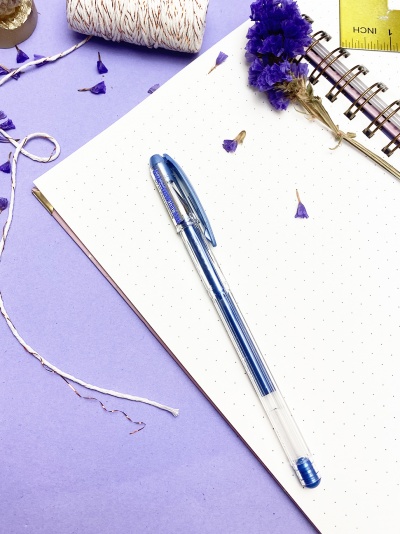 Caderno pontilhado com caneta azul e flores secas sobre fundo lilás