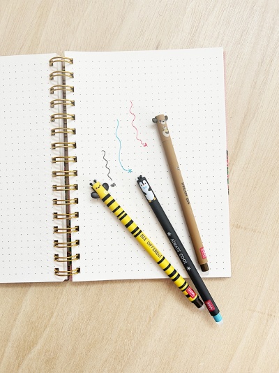 Três canetas decorativas coloridas sobre caderno espiral aberto com folhas pontilhadas.