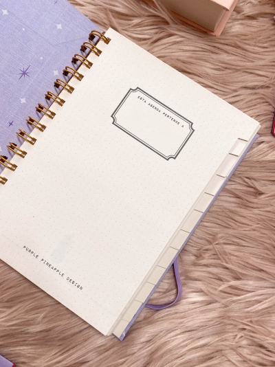 Caderno roxo com estrelas e páginas internas com abas numéricas sobre superfície felpuda bege