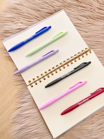 Caderno aberto com seis canetas coloridas alinhadas sobre as páginas