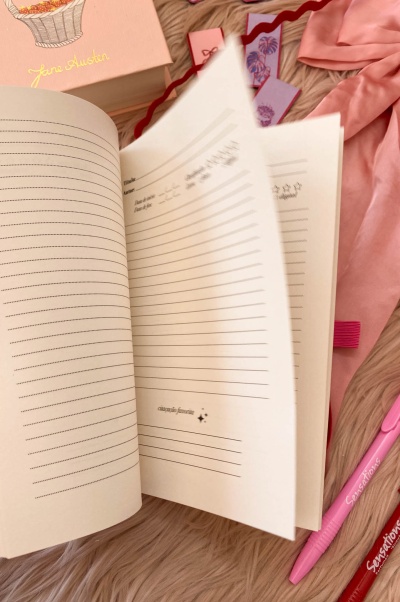 Caderno aberto com páginas pautadas e caixa rosa Jane Austen ao fundo