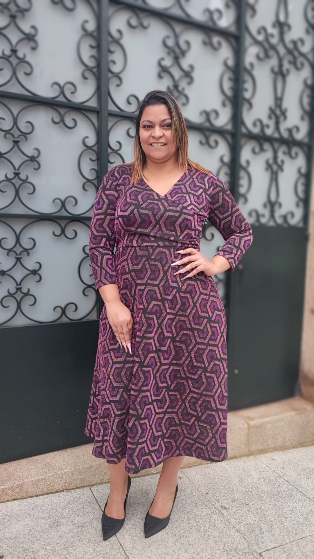 Vestido com padrão e brilho Vestido comprido estampado em tons roxos com sapatos pretos e portão de ferro ao fundo