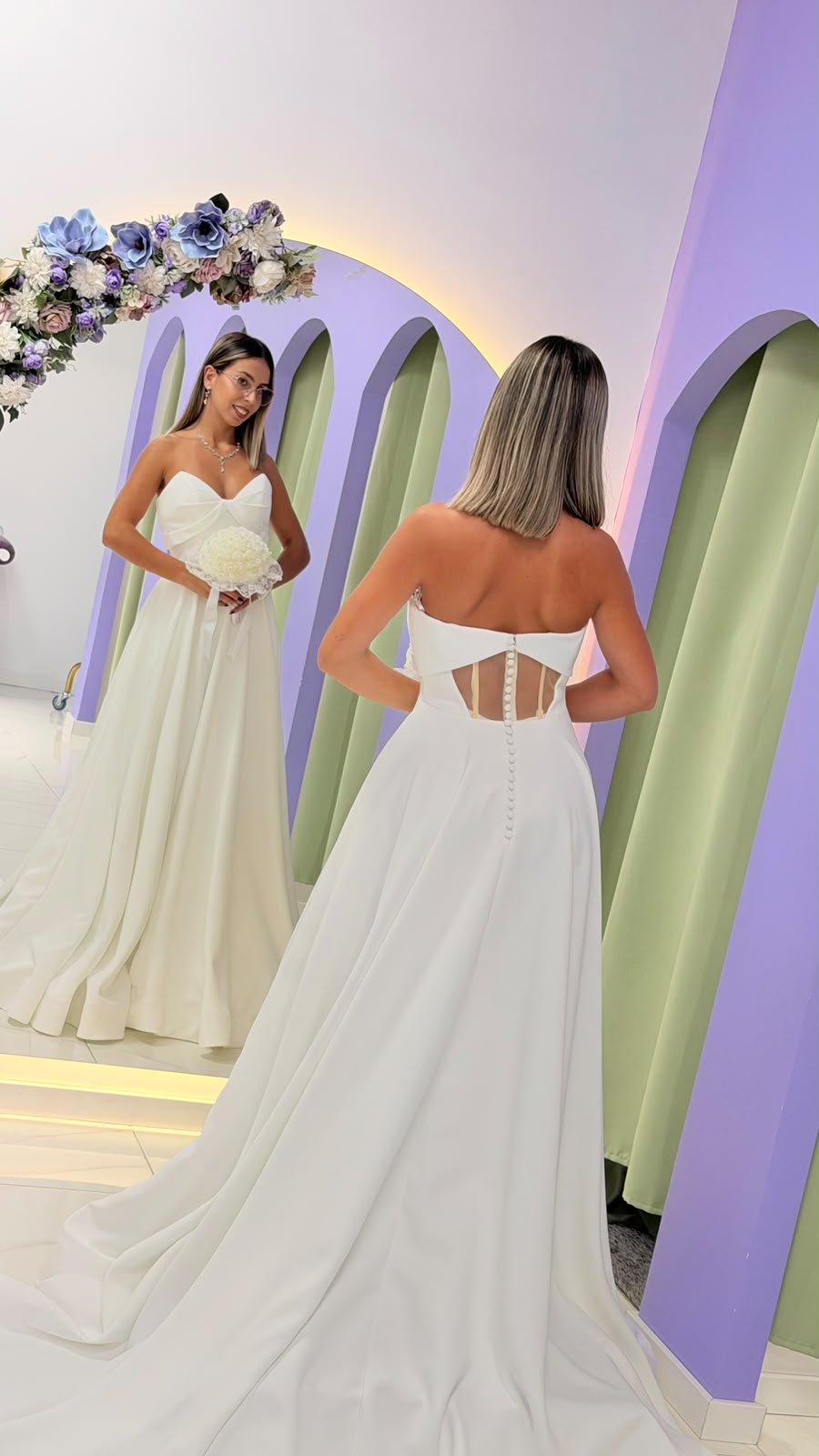 Vestido Celine Noiva Vestido de noiva branco com detalhes de botões visto de costas refletido num espelho em moldura lilás