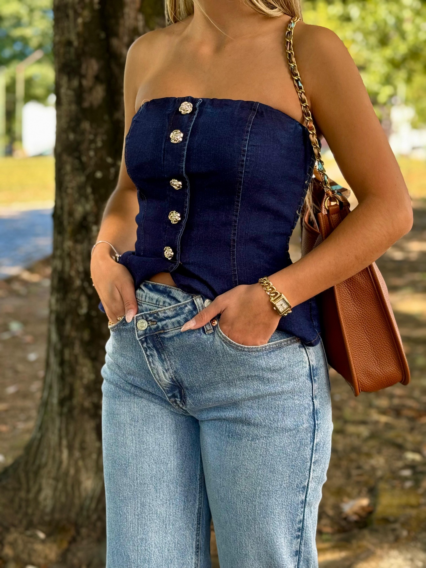 Calça de Ganga Foly Top feminino azul escuro com botões e calças de ganga claras junto a árvore.