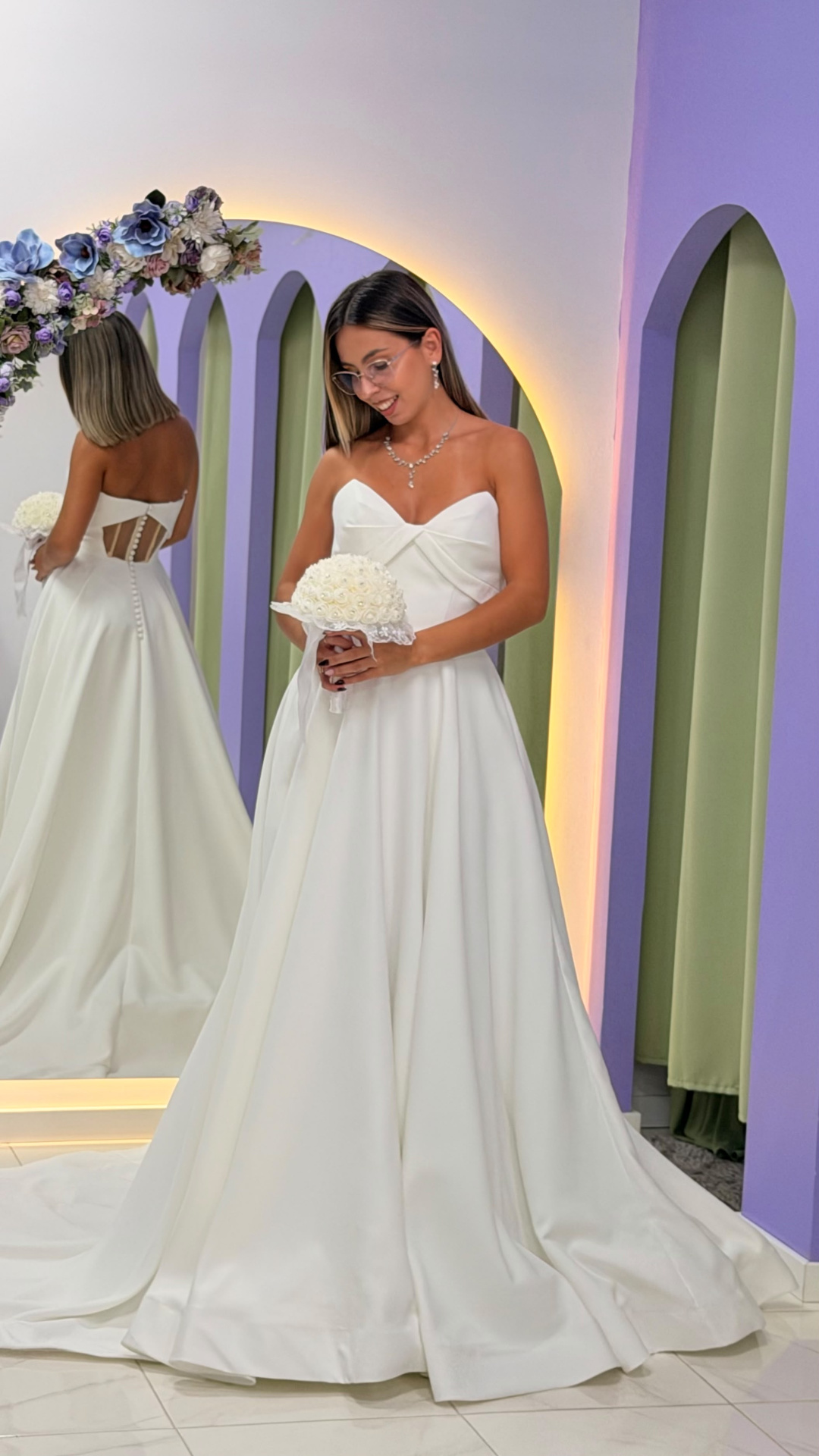 Vestido Celine Noiva Vestido de noiva branco tomara que caia com recortes e botões nas costas, mulher com bouquet branco e acessórios cristais