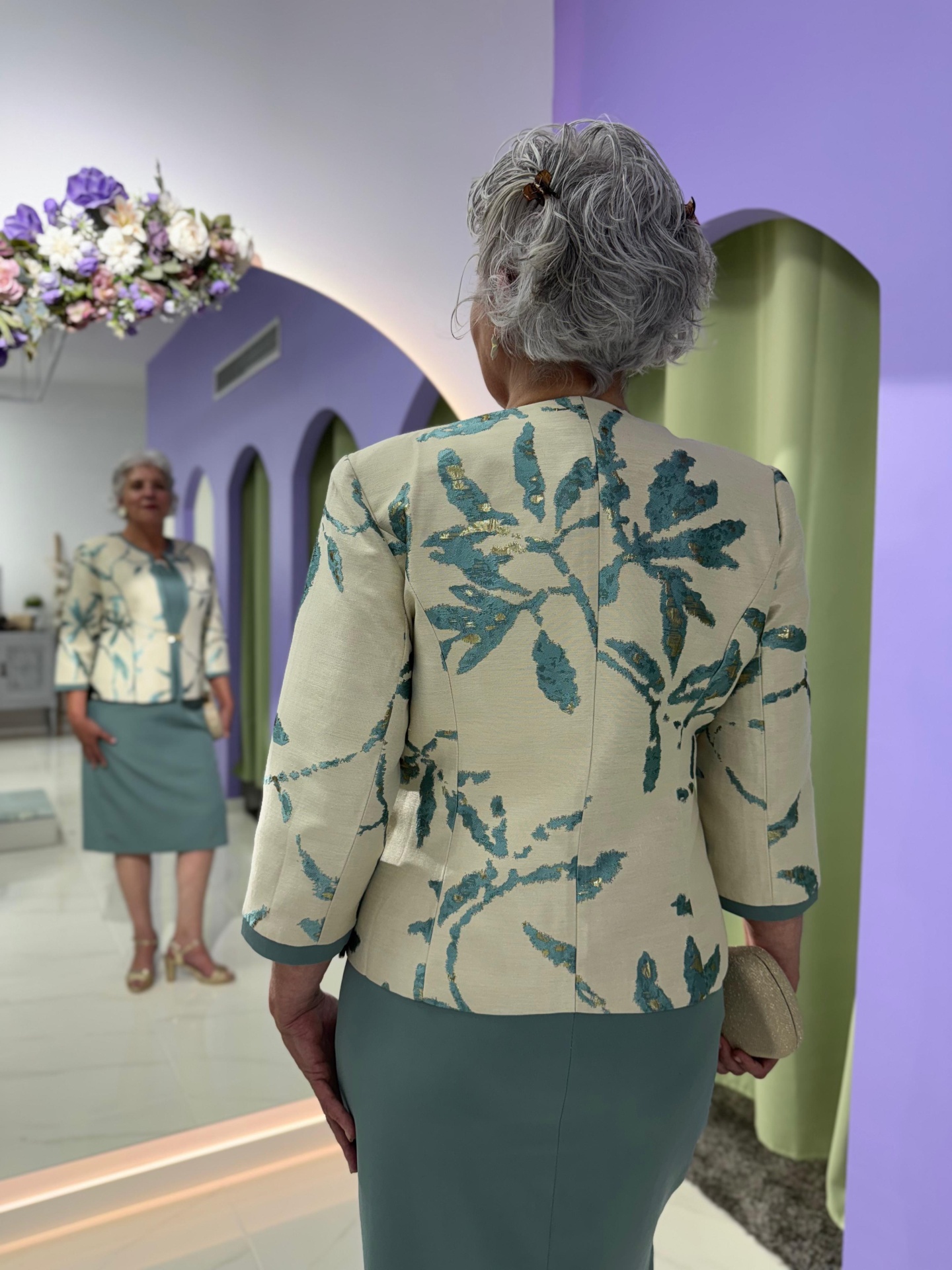 Conj. Casaco + Vestido Serena Casaco bege com padrão de folhas azuis e saia verde numa sala com paredes lilás