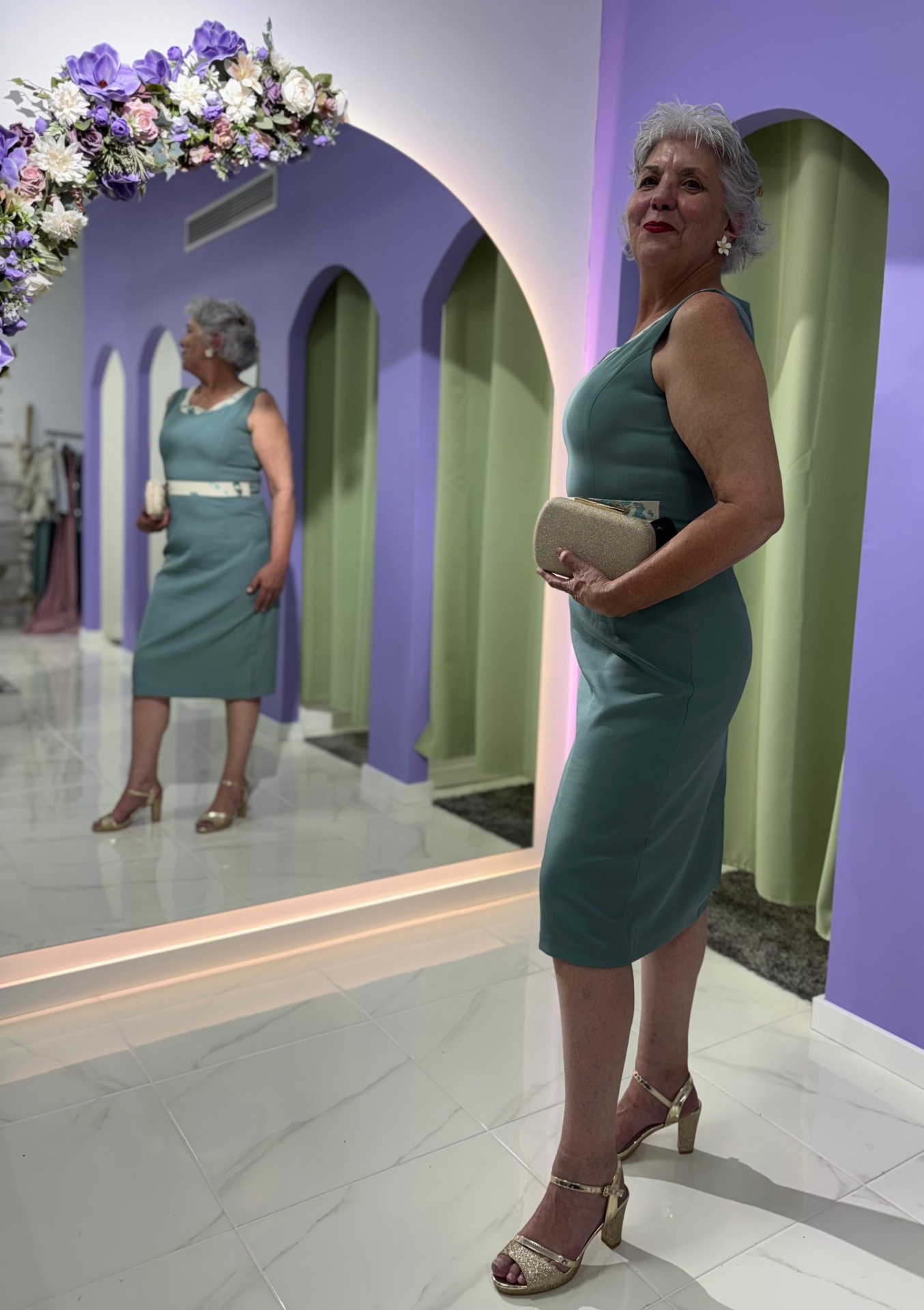 Conj. Casaco + Vestido Serena Mulher com vestido verde-azulado e mala bege em interior com espelho e flores