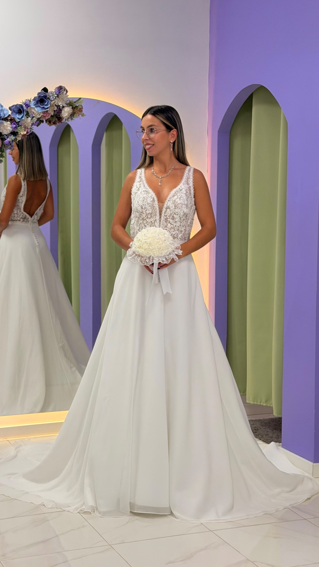 Vestido Miriam Noiva Vestido de noiva branco com corpete em renda e saia ampla em cenário com arcos lilás e verde