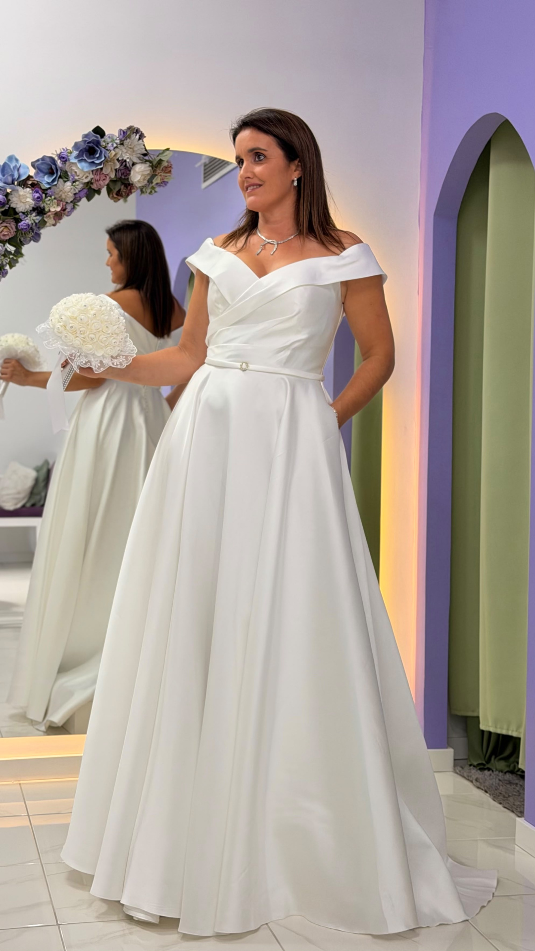 Vestido Gabrielle Noiva Vestido de noiva branco ombro a ombro com bouquet branco, interior com espelho e flores decorativas.