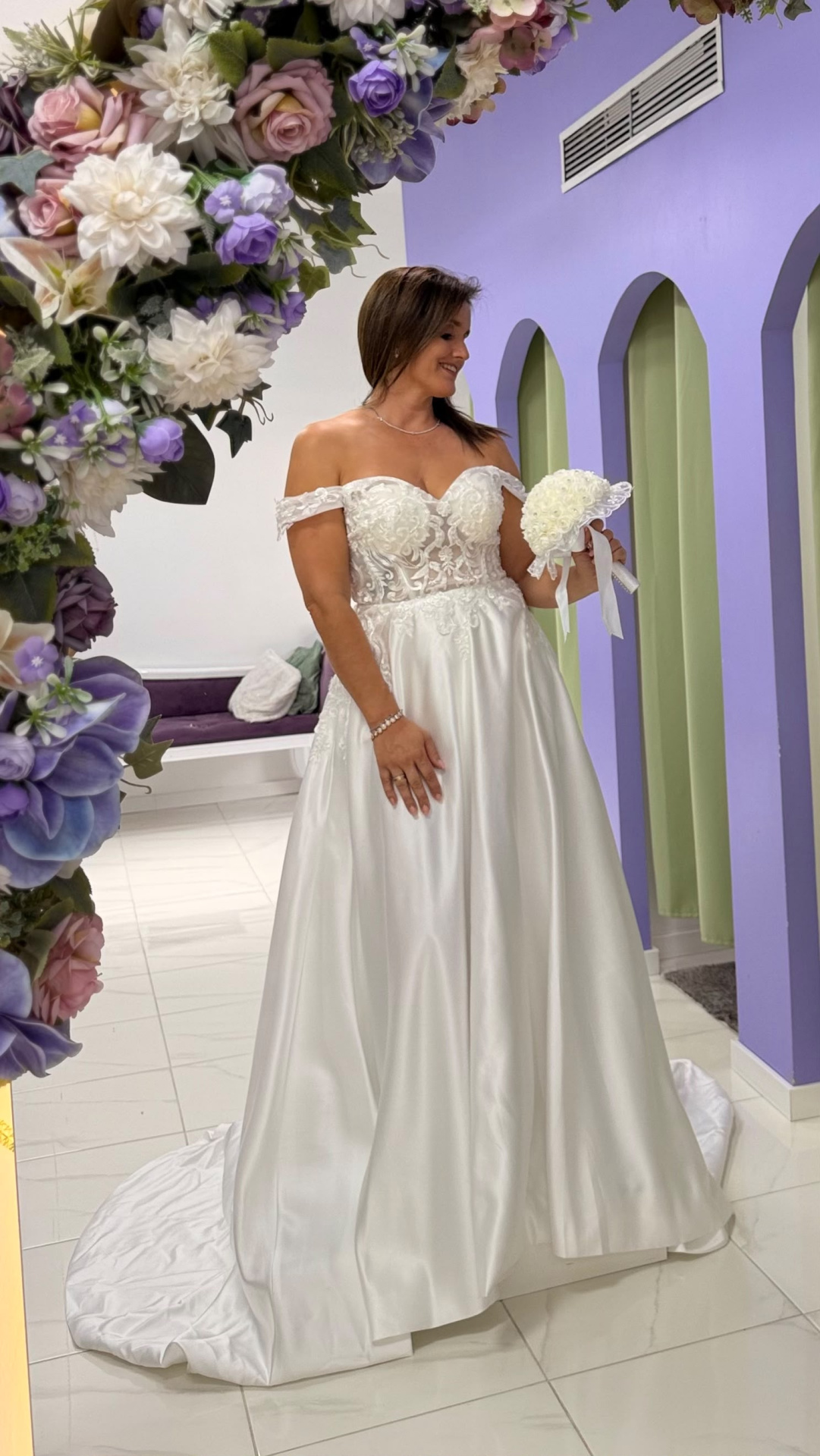 Vestido Amour Glamour Vestido de noiva branco bordado com bouquet em ambiente com arcos lilás e flores artificiais