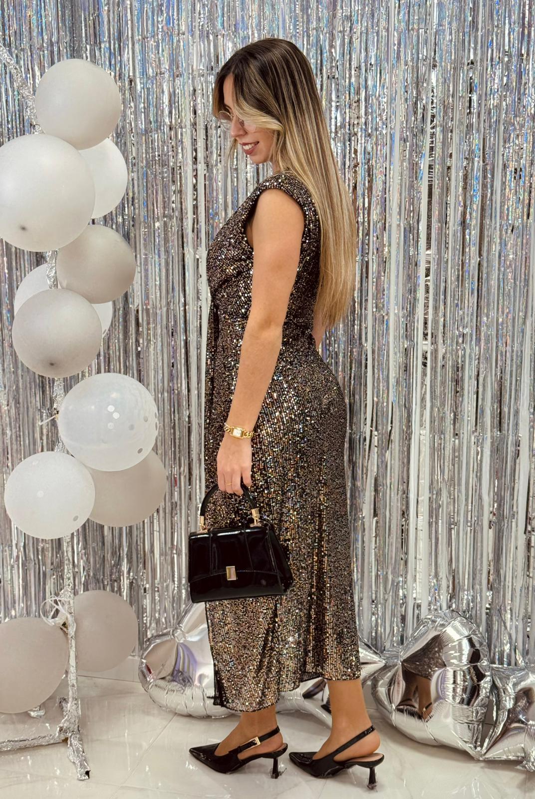 Vestido Luna Mulher a usar vestido brilhante prateado com sapatos pretos e mala, fundo prateado e balões brancos