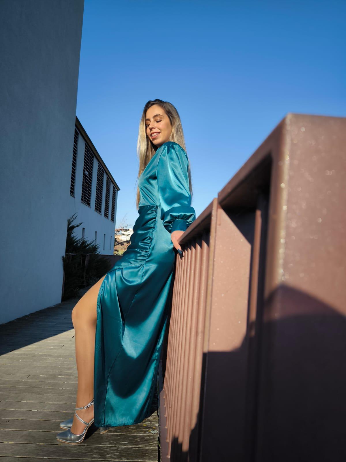 Vestido comprido c/ manga em cetim Mulher a usar vestido azul cintilante comprido com fenda e sandálias prateadas ao ar livre